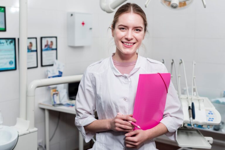 A dental office administrator holding a file and standing in front of dental equipment