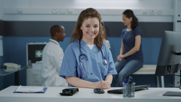 Portrait of woman Medical Office Assistants and wearing uniform in office, sitting at desk. Medical assistant with stethoscope looking at camera and getting ready to help doctor at appointment.